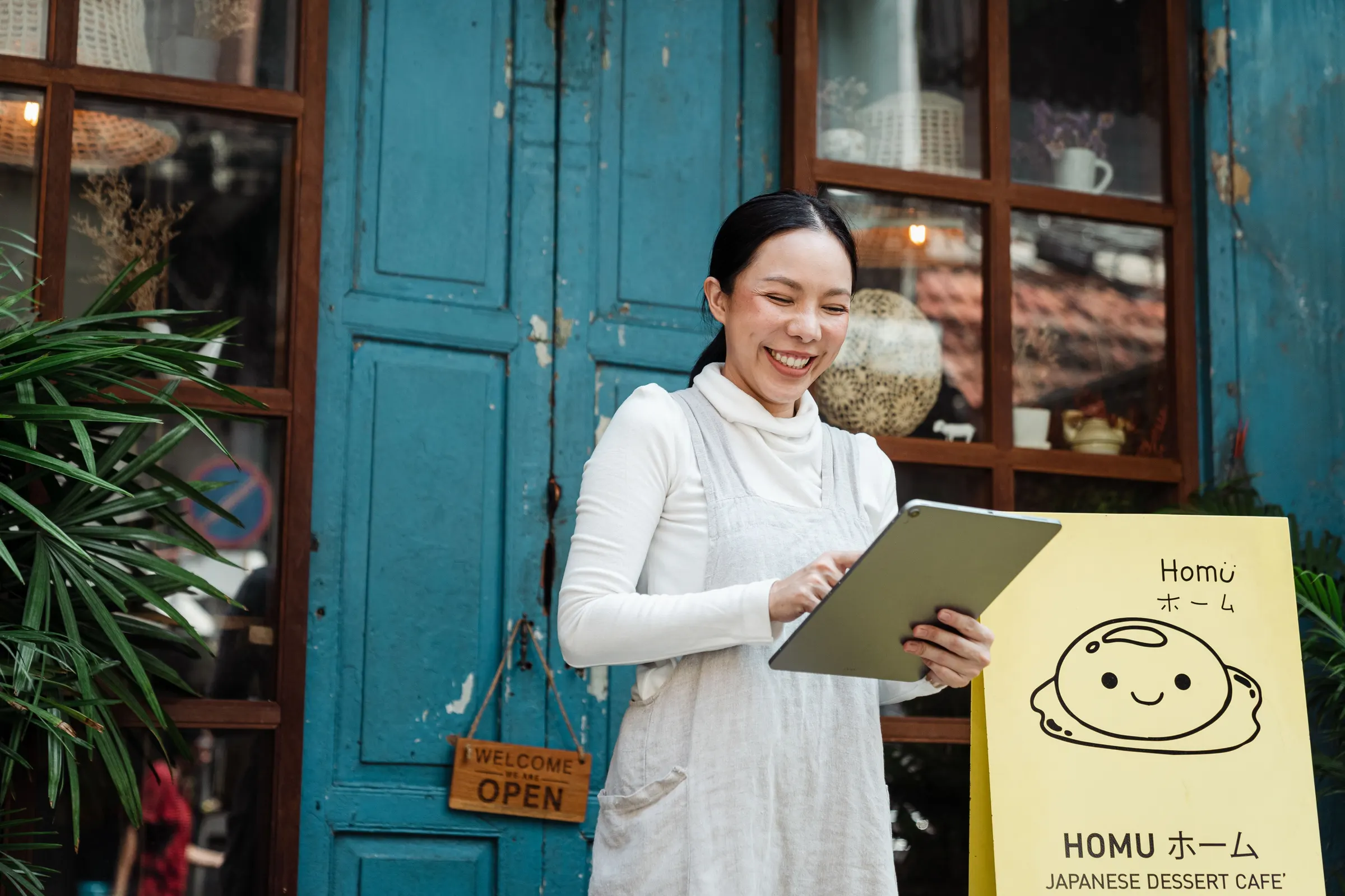 A smiling shop owner checking bookings on a tablet outside her cafe